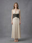 Woman in a cream satin maxi dress with black lace waist detail, standing against a grey backdrop.
