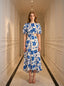 Woman wearing a white and blue floral print midi dress with cut-out waist and puff sleeves, standing in a hallway.