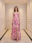 Woman wearing a pink floral print maxi dress with spaghetti straps and a high slit, standing in a hallway.