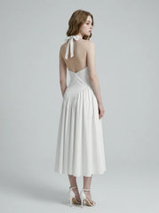 Back view of a woman in a white halter neck midi dress, showing the open back and tie closure.