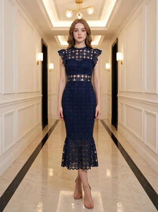 Woman wearing a navy blue lace mermaid dress with a high neck and cap sleeves, standing in a hallway.