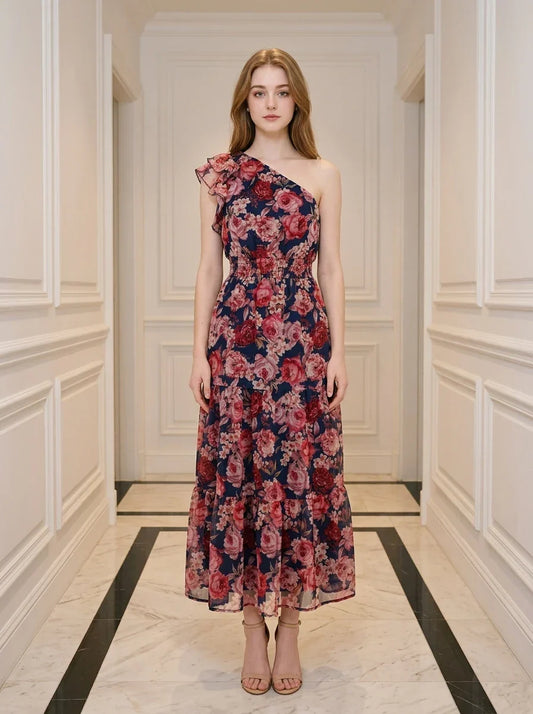 Woman wearing a navy floral print one-shoulder dress with a tiered skirt and ruffle detail, standing in a hallway.