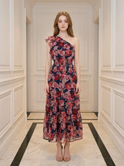 Woman wearing a navy floral print one-shoulder dress with a tiered skirt and ruffle detail, standing in a hallway.