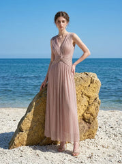 Woman in a rose gold shimmering metallic A-line V-neck sleeveless floor-length formal gown, standing on a beach