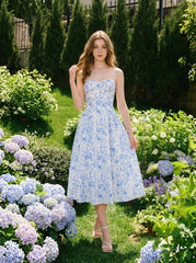 Woman wearing a blue and white floral print midi dress with spaghetti straps, standing in a garden with hydrangeas.