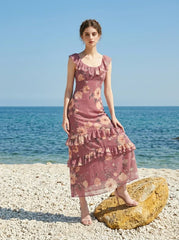 Woman wearing a pink floral print maxi dress on a beach with rocks and the ocean