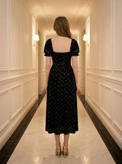 The back of a woman wearing a black velvet midi dress with a floral print.