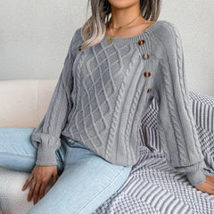 Woman wearing a grey cable knit sweater with buttons, sitting on a couch with a blanket, paired with light wash jeans.