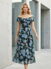 Woman standing in an urban setting wearing a black off-the-shoulder midi dress with a blue floral print