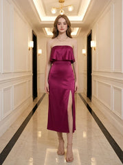 Woman wearing a strapless magenta satin midi dress with a high slit, standing in a hallway.