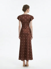 Back view of a woman wearing a brown polka dot midi dress with ruffled sleeves and a v-neckline, standing against a white background.