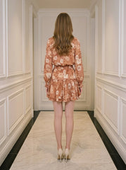 Back view of a woman wearing a floral print mini dress with long sleeves and a V-neck.