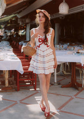 Woman wearing a white mini dress with red trim and bows, a straw hat, and red shoes, holding a wicker basket.