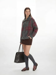Side profile of a woman in a grey plaid knit jacket, brown mini skirt, and grey knee-high socks, carrying a black handbag.