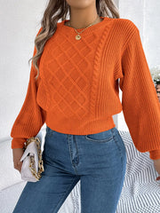 Woman wearing an orange cable knit sweater, blue jeans, and holding a white handbag