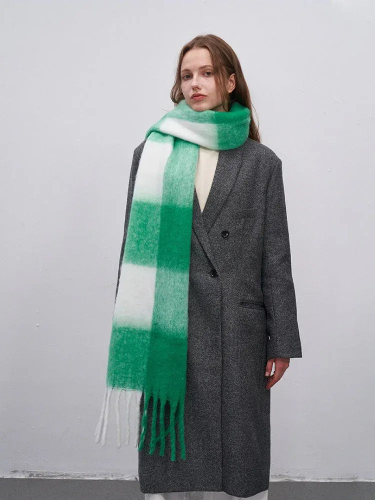 Woman in a grey coat with a large green and white plaid scarf draped around her neck.