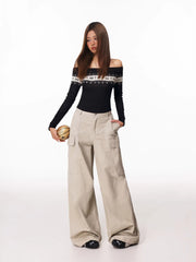 Full-body shot of a woman in a black off-the-shoulder knit top with a decorative yoke and loose-fitting beige cargo pants.