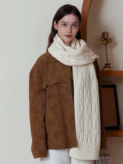 Woman wearing a long, cream-colored cable knit scarf draped over a brown jacket.