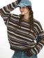 Model posing with hand on head, wearing a striped sweater and blue cap.