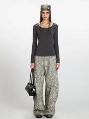 Woman wearing a dark grey long-sleeve top with a square neckline and button details, paired with wide-leg grey leopard print pants and a dark handbag. She is also wearing a patterned headscarf.