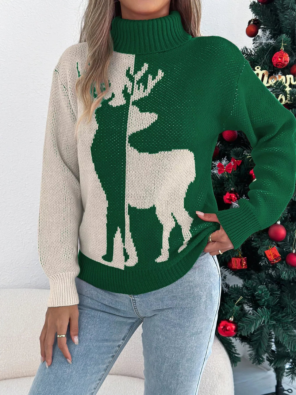 Woman posing in a green and cream knit sweater with a reindeer graphic and a turtleneck.