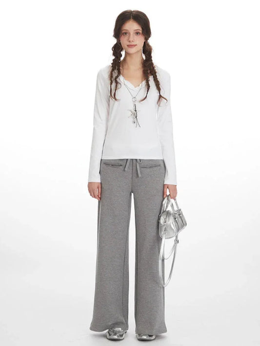 Woman wearing a white long-sleeve shirt and grey wide-leg sweatpants, holding a silver handbag.
