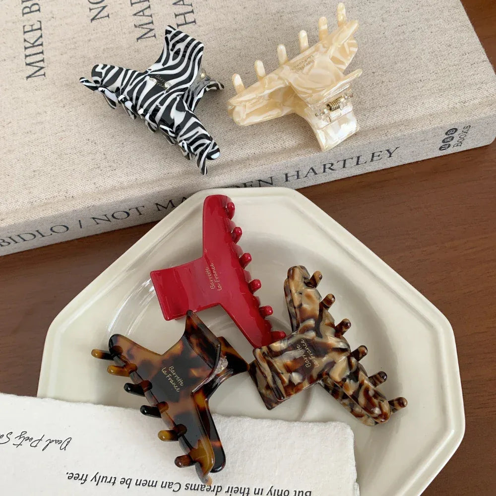 A close-up of four hair claw clips arranged on a white plate. Patterns include zebra print, red, tortoiseshell, and a marbled brown.