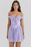Woman wearing a lavender off-the-shoulder mini dress with a draped bodice and pleated skirt, front view.