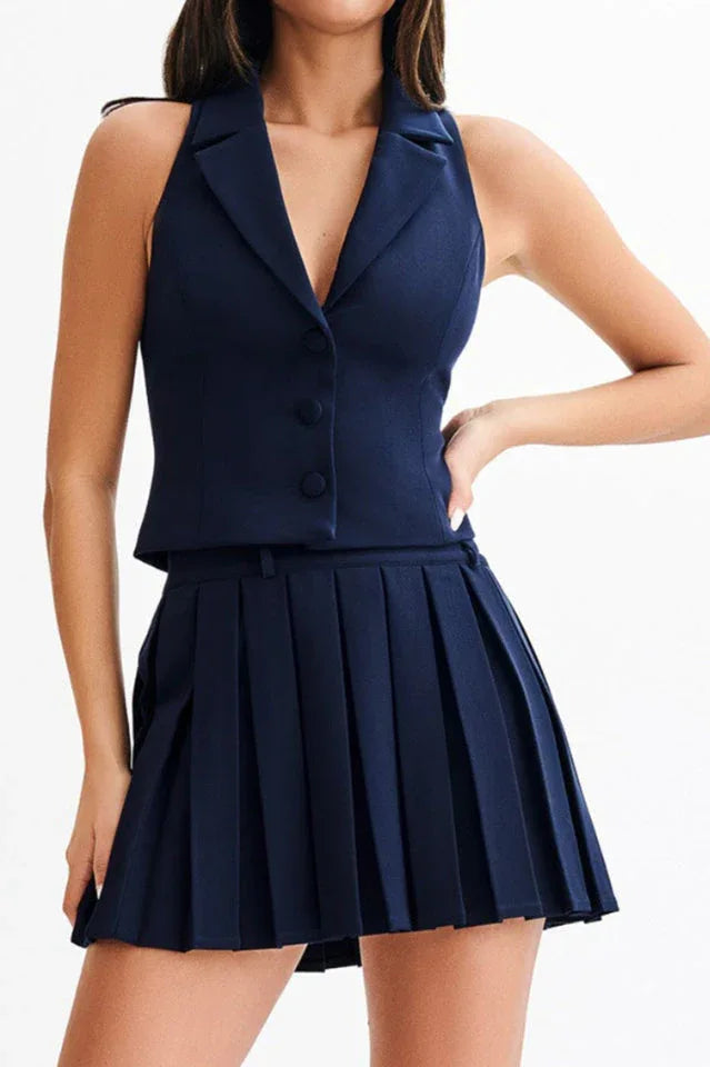 Woman wearing a navy blue sleeveless blazer vest and pleated skirt.
