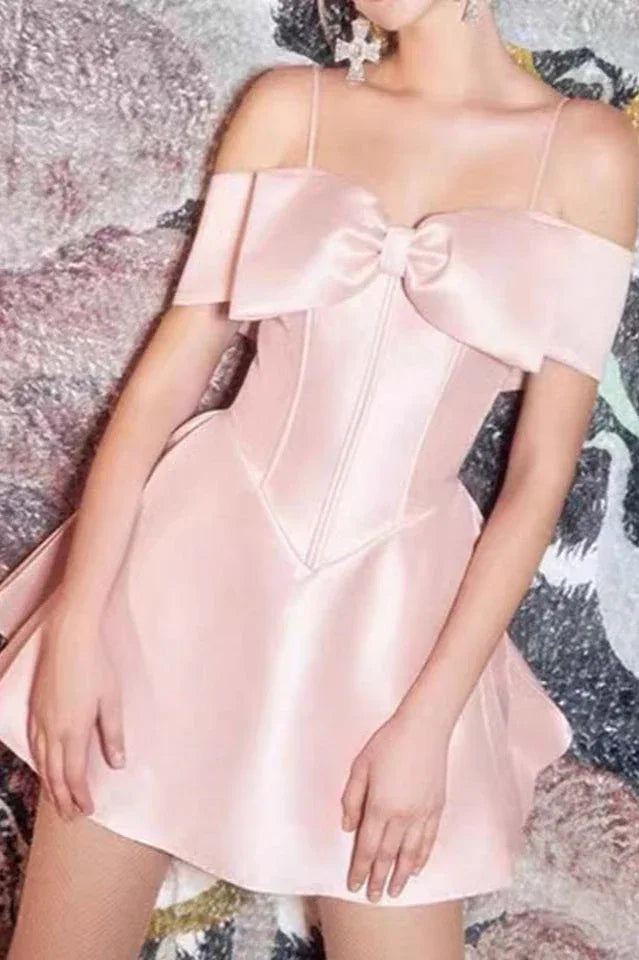 Close-up of a woman's torso in a pale pink satin off-the-shoulder dress with a bow accent and corset-style bodice.
