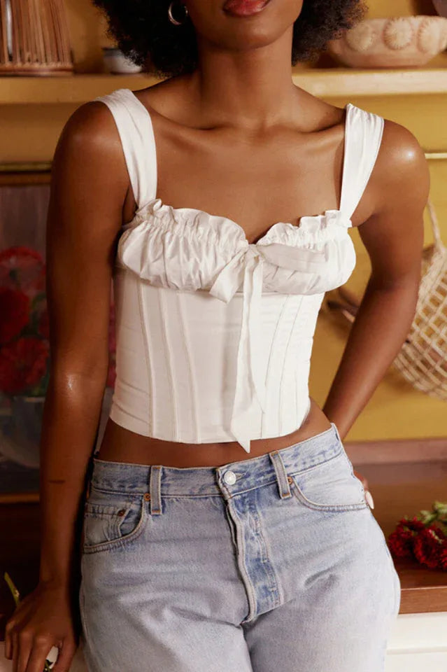 Close-up of a woman wearing a white ruched corset top with a bow accent and light wash denim jeans.