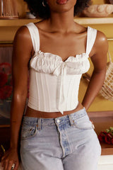 Close-up of a woman wearing a white ruched corset top with a bow accent and light wash denim jeans.