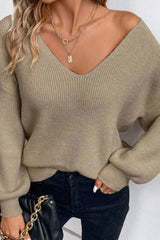 Close-up of a woman wearing a light brown V-neck knit sweater with lantern sleeves and black jeans