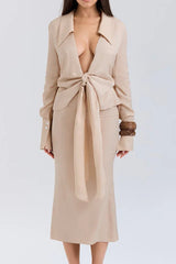 Woman wearing a beige linen blend long-sleeved top with a deep V-neckline and front tie closure, paired with a matching midi skirt.