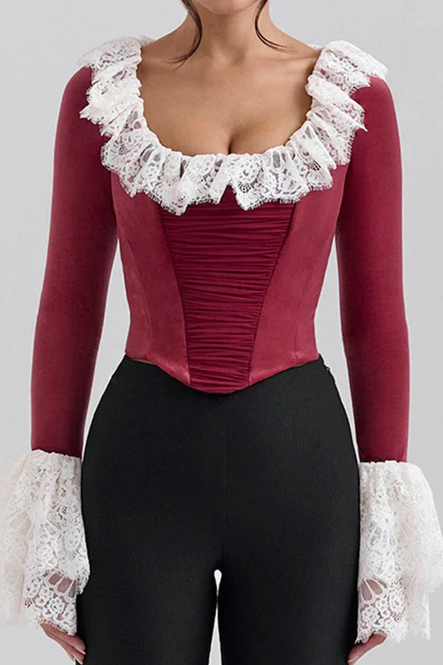 Woman wearing a red velvet top with white lace trim and ruffled collar and cuffs, front view