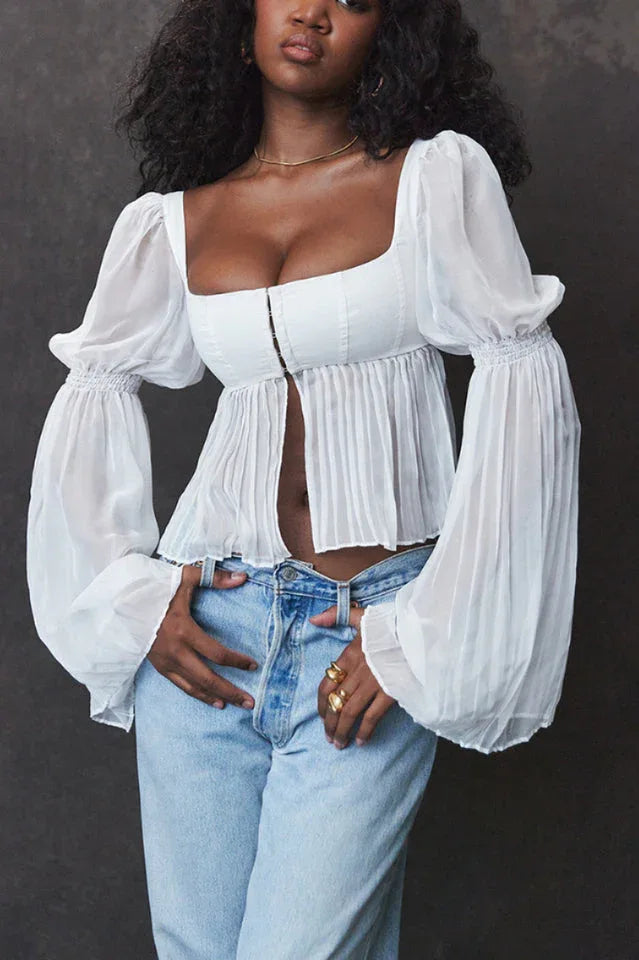 Woman with dark curly hair wearing a white cropped blouse with a square neckline and sheer bell sleeves