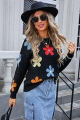 Woman wearing a black long-sleeve sweater with a colorful floral print, denim skirt, black hat, and sunglasses.