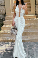 Woman wearing a white halter neck maxi dress with a plunging neckline and ruched detailing, holding a small handbag.