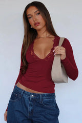 Woman wearing a burgundy long-sleeve top with lace trim, dark wash jeans, and a beige shoulder bag, showing accessories.