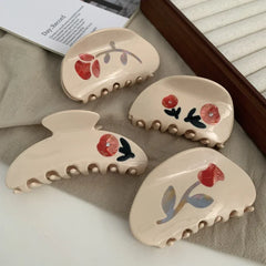 A collection of cream-colored claw clips with red floral designs.