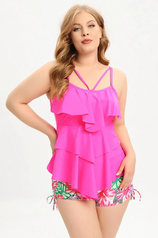 Woman wearing a bright pink ruffled tankini top with floral print swim shorts, front view.