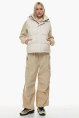 Woman wearing a cream puffer vest, cream hoodie, and tan cargo pants, hands in pockets