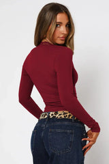 Back view of a woman wearing a burgundy long-sleeve top with lace trim and dark wash jeans.