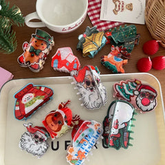 Assortment of holiday-themed hair claw clips displayed on a white tray and a wooden table, featuring gingerbread men, Santas, and snowmen.