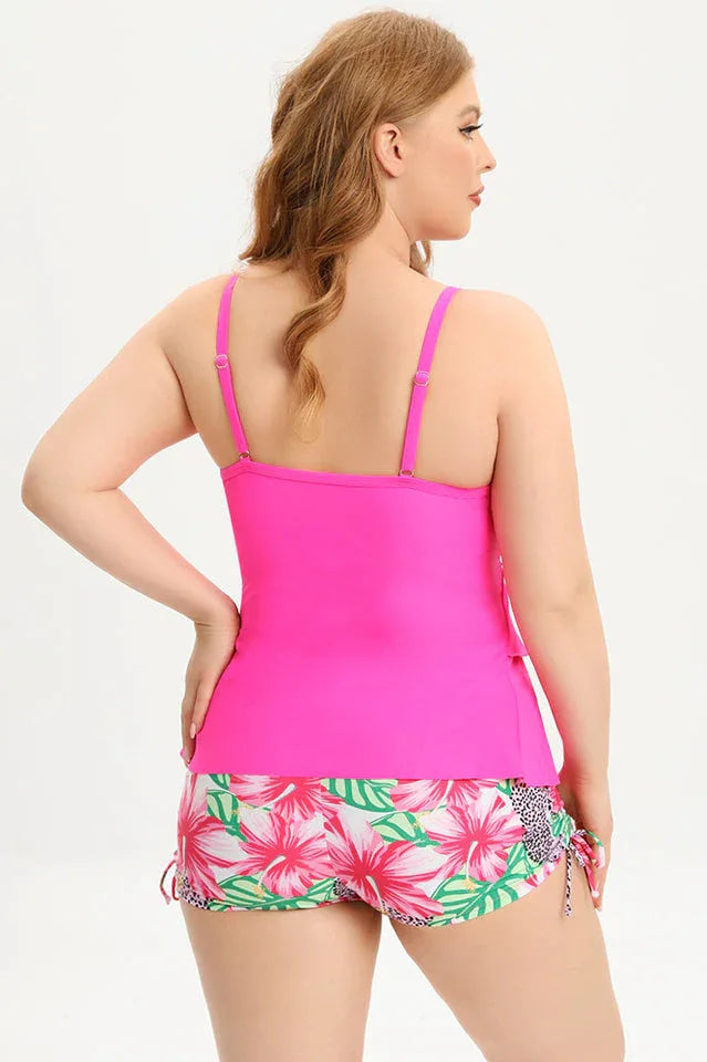 Woman wearing a bright pink ruffled tankini top with floral print swim shorts, back view.