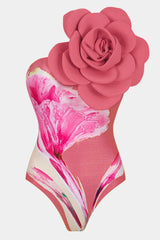 Close-up of a pink one-piece swimsuit with a floral print and a large 3D flower embellishment on the shoulder.