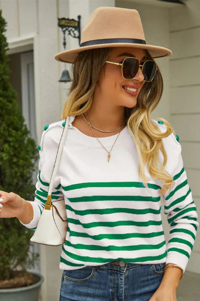 Woman wearing a white and green striped knit sweater with a crew neck and button details on the shoulders, paired with blue jeans and a tan fedora hat.