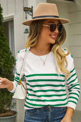 Woman wearing a white and green striped knit sweater with a crew neck and button details on the shoulders, paired with blue jeans and a tan fedora hat.