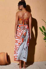 Back view of a woman wearing an orange one-shoulder bikini top and a matching sarong