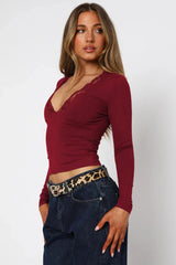 Side view of a woman wearing a burgundy long-sleeve top with lace trim, dark wash jeans, and a leopard print belt.